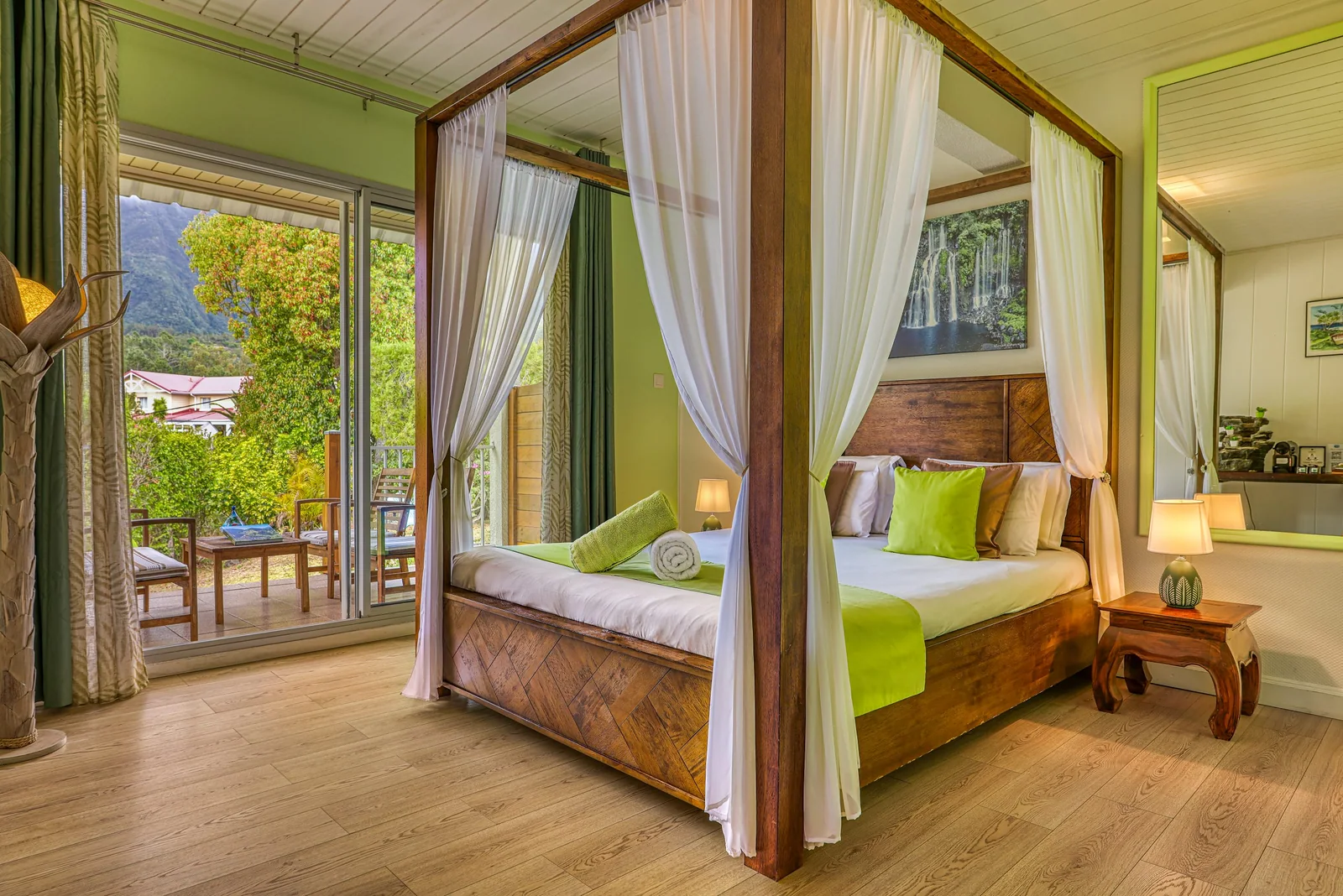 Le lit à baldaquin de la chambre Langevin, voilages blancs et coussins vert anis, face à la porte-fenêtre